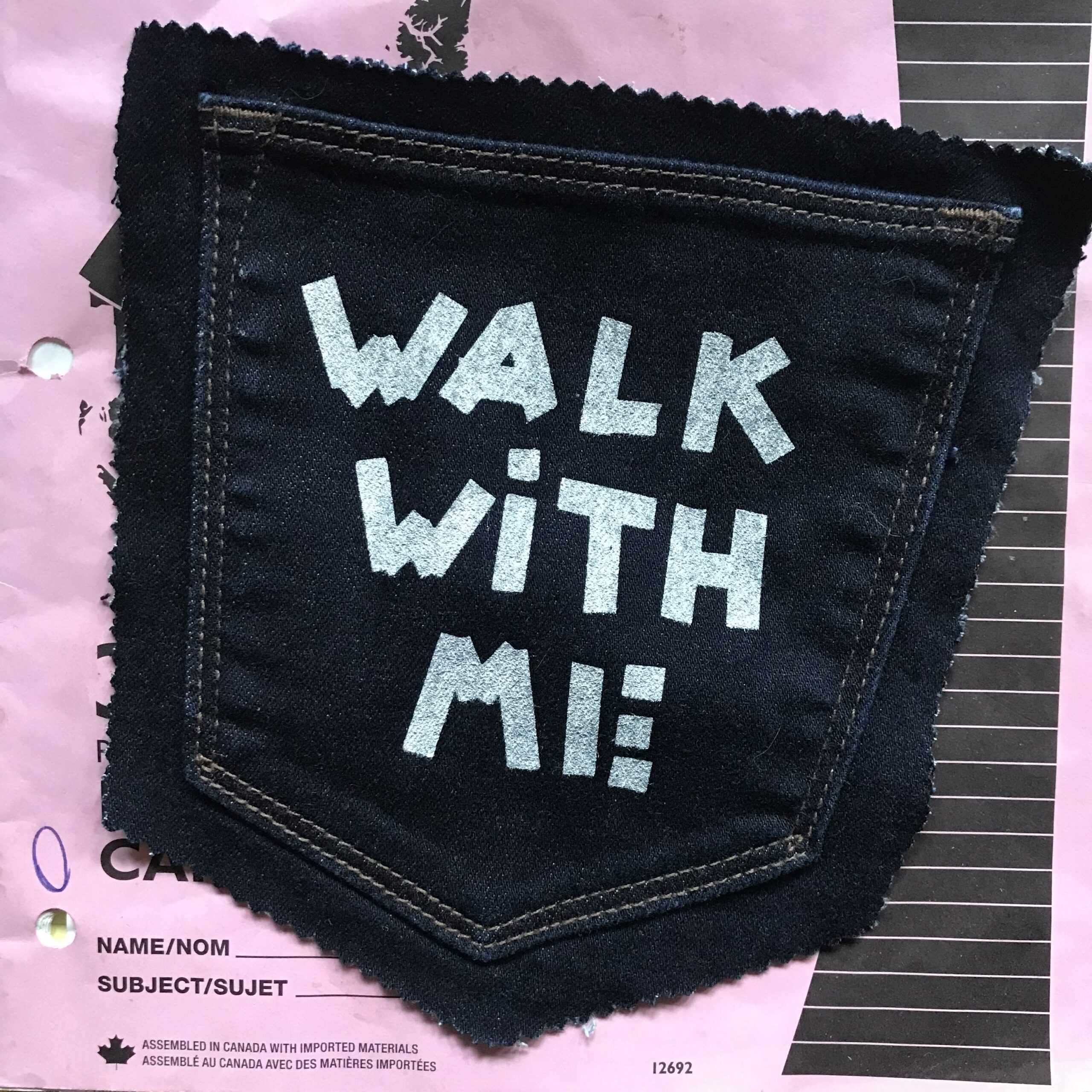A patch reading "walk with me" promoting an exhibition at the Campbell River Art Gallery.