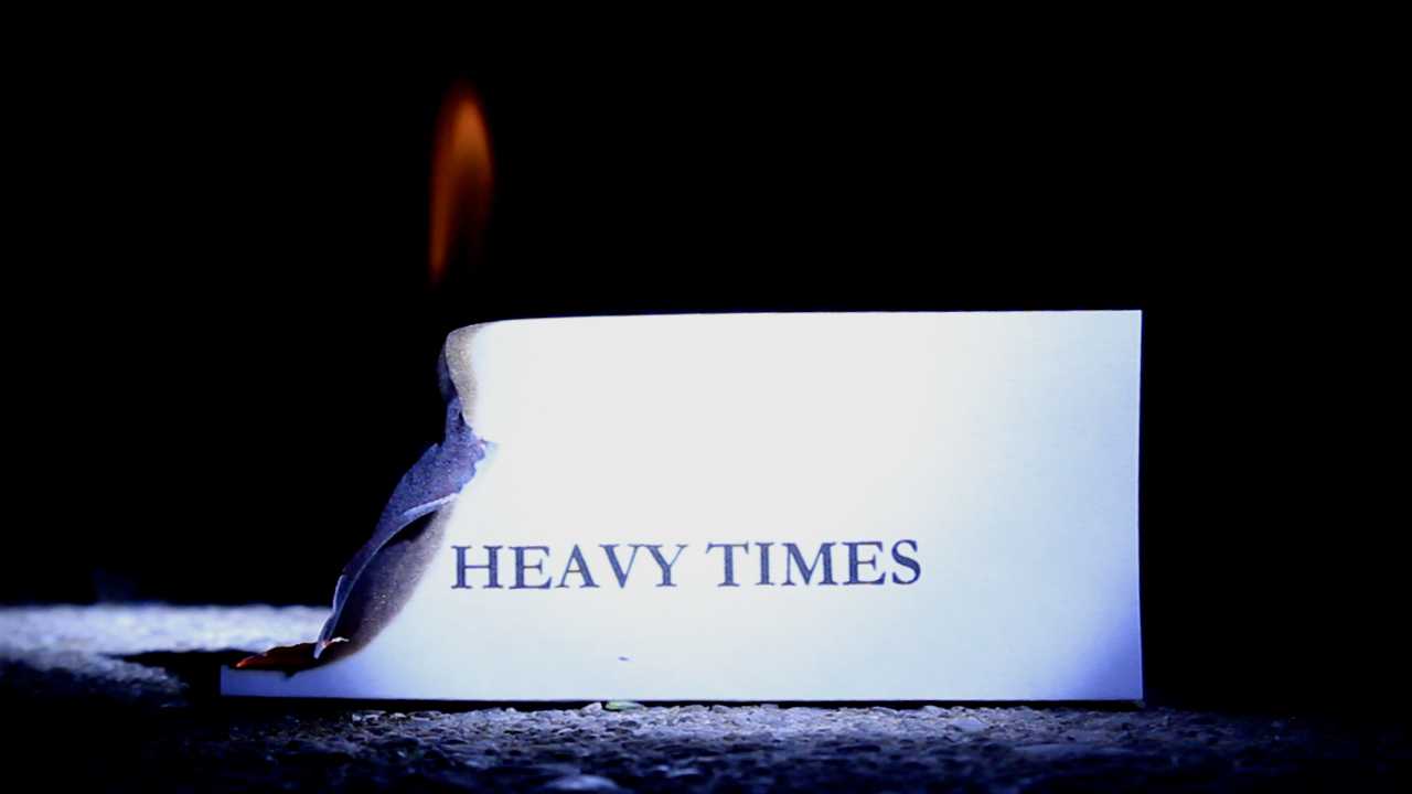 Still of a burning piece of paper that reads “heavy times”