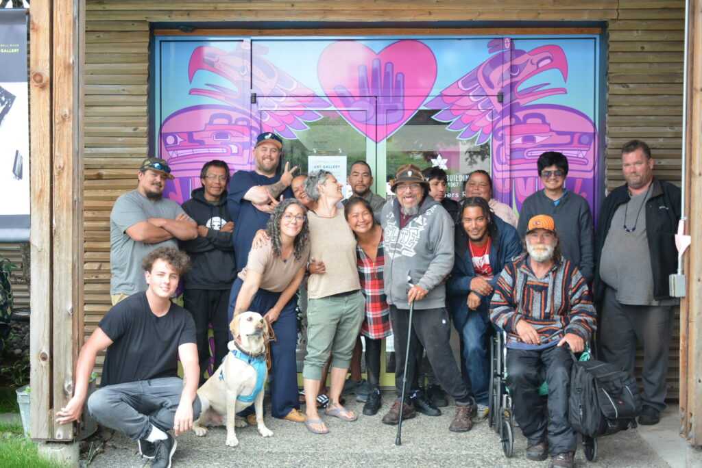 Group photo of smiling people and one dog, standing in front of a mural
